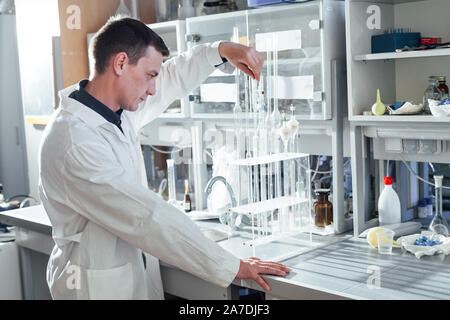 Scienziato maschio conduce esperimenti di chimica con fluidi nel laboratorio di analisi mediche Foto Stock