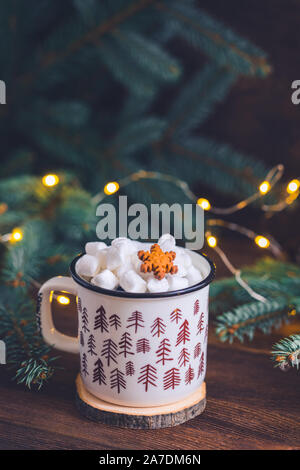 Abete colorato tazza ceramica con un caffè o una cioccolata calda con marshmallows sul luminoso sullo sfondo di legno con scintillante garland Foto Stock