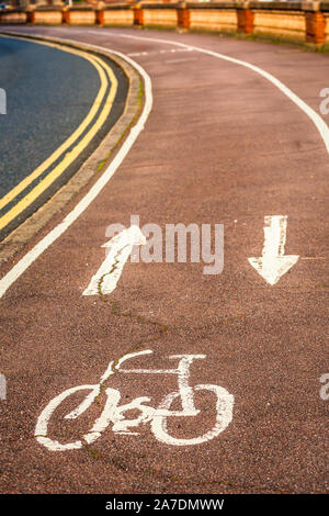 Icona di biciclette dipinte di vernice bianca su di una pista ciclabile con due frecce che si arriccia in soft focus in distanza. Foto Stock