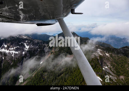 Vista dall'ala di aeroplano dalla finestra volando sopra la Howe Sound montagne durante un nuvoloso mattina d'estate. Prese a nord di Vancouver, British col Foto Stock
