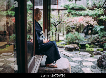 Uomo giapponese meditando nel suo giardino Foto Stock