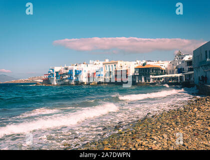 Le onde del mare la creazione di schiuma di latte in primo piano con edifici bianchi in background mykonos grecia Foto Stock