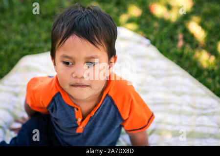 Un piccolo ragazzo seduto in una coperta picnic cercando triste e riflessivo. Foto Stock