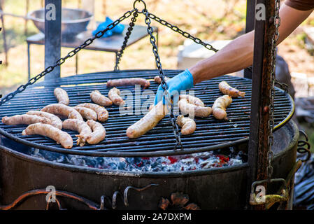 Maschio di chef preparare le salsicce sul barbecue grill, street food, estate food festival. Salsiccia fresca e hot dogs grigliare all'aperto su un barbecue. Foto Stock