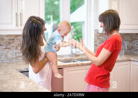 Il concetto di maternità, nanny, l'infanzia e la fanciullezza. Piscina shot in cucina. Due donne e un bambino in braccio, una famiglia felice Foto Stock