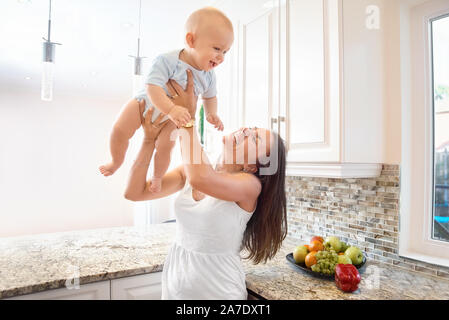 Il concetto di maternità, nanny, l'infanzia e la fanciullezza. Piscina shot in cucina. donne e un bambino in braccio il bambino getta fino al ceili Foto Stock
