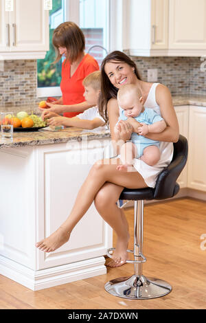 Il concetto di maternità, nanny, l'infanzia e la fanciullezza. Piscina shot in cucina. Due donne e un bambino in braccio, guardando verso la fotocamera e s Foto Stock