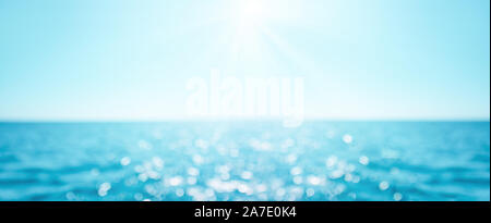 Bella la sfocatura defocalizzata mare azzurro sfondo con raggi di sole e bokeh di fondo. Paesaggio di estate tropicale. La vacanza estiva concept Foto Stock