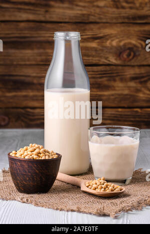 Bottiglia di latte di soia con fagioli di soia sul tavolo bianco più scuro dello sfondo in legno Foto Stock