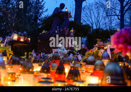 Candele accese illuminano una statua del Santo Padre Giovanni Paolo II durante la celebrazione della festa di Tutti i Santi al cimitero Rakowicki. Il 1 novembre è un giorno di riposo dal lavoro e persone visitano le tombe dei loro cari. Foto Stock