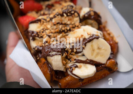 Mano che tiene in casa cialde belghe con il miele, banana, fragola e cioccolato di sfondo Foto Stock