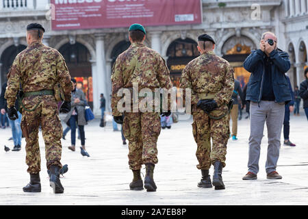 Venezia, Italia - 20 Marzo 2015:vista posteriore di tre anonimo di uomini in uniforme militare camminare vicino a turistico con foto fotocamera mentre il pattugliamento Piazza San Foto Stock