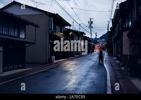 Takayama, Giappone - Aprile 8, 2019: Città nella Prefettura di Gifu nel tradizionale villaggio di notte con la lanterna accesa lampade e donna attraversamento strada Foto Stock