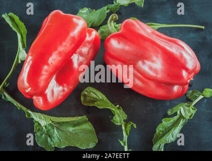 Res peperoni e foglie di rucola su un nero sfondo rustico. Cibo scuro Foto Stock