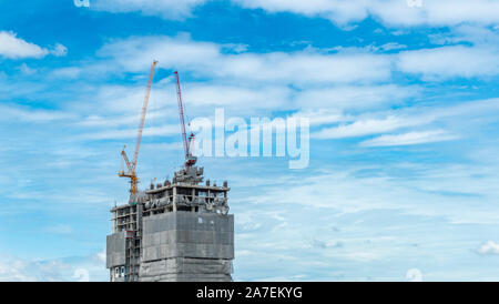 Gru a lavorare sulla parte superiore dell edificio, stand alone edificio, cielo blu e nuvole sullo sfondo Foto Stock