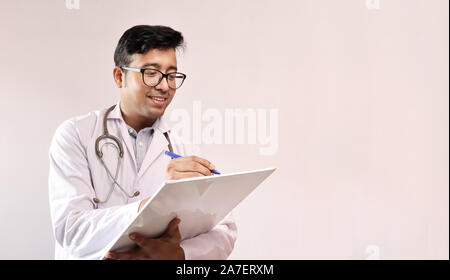 Indiano maschio medico in camice bianco e stetoscopio scrivere note e prescrivere medicine Foto Stock