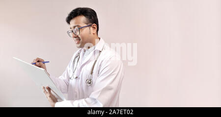 Indiano maschio medico in camice bianco e stetoscopio scrivere note e prescrivere medicine Foto Stock