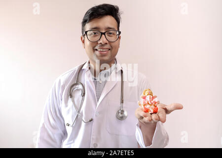 Indiano maschio medico in camice bianco e stetoscopio con una statua del signore ganesha in mano, medico la fede in Dio immagine Foto Stock
