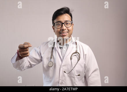 Indiano maschio medico in camice bianco e stetoscopio che mostra segni di denaro Foto Stock