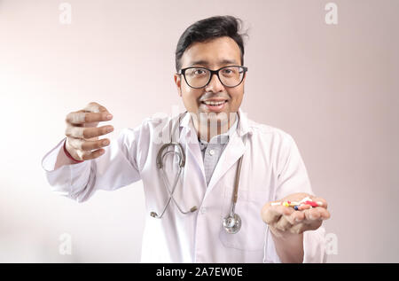 Indiano maschio medico in camice bianco e lo stetoscopio con la medicina pillole compresse capsule in mano e che mostra segni di denaro Foto Stock
