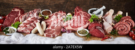 Ampia selezione di materie prime fresche per un barbecue di inverno in un panorama con carne di maiale, carne di manzo e di pollo, bistecche e salsicce in una fila sulla neve con erbe fresche e sp Foto Stock