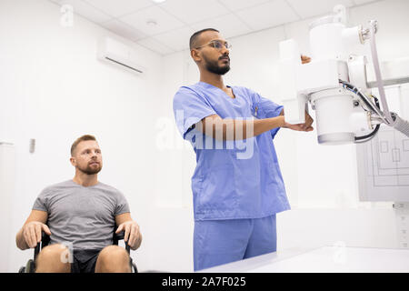 Giovane atleta sulla sedia a rotelle guardando medico test di nuove attrezzature mediche Foto Stock