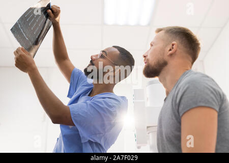 Radiologo e il suo paziente guardando a raggi x del cardano rotto detenute dal medico Foto Stock