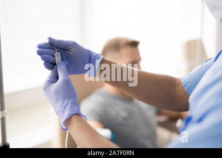 Le mani del medico guanti parte di ritegno di un contagocce con la medicina per uno dei pazienti Foto Stock