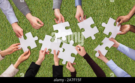 Una vista aerea di persone mani unendo il bianco i puzzle su erba verde Turf Foto Stock