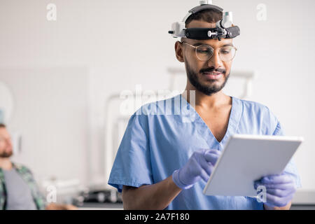 Medico in uniforme e apparecchiature mediche sulla testa a scorrere attraverso i dati online Foto Stock