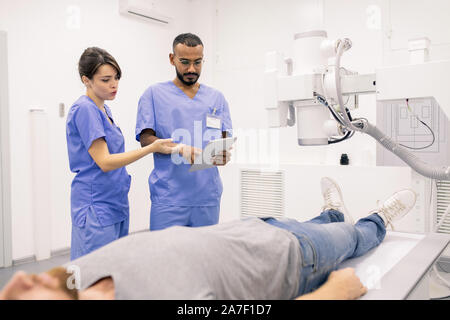 Due giovani medici in uniforme blu per discutere i dati online in touchpad Foto Stock