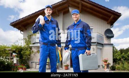 Ritratto di sorridere due giovani elettricista maschio in piedi di fronte a casa con i kit elettricista Foto Stock