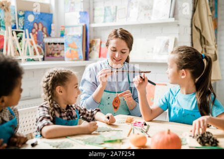 Felice giovane insegnante che mostra un gruppo di schoolkids zucca di Halloween decorazione Foto Stock