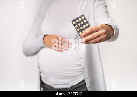 Irriconoscibile la donna incinta che mostra le pillole che posano su sfondo bianco, tagliato Foto Stock