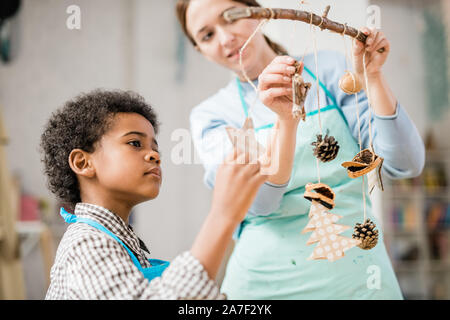 Carino boy guardando uno dei fatti a mano decorazioni di Natale appeso su stick Foto Stock