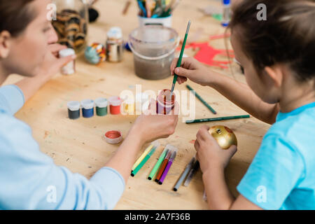 Creative schoolgirl con pennello prendendo un po' di vernice dal piccolo vaso in plastica Foto Stock