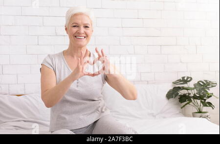 Carino donna senior messa a forma di cuore con le sue mani e dita Foto Stock