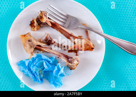 Piastra bianca con mangiato Pollo gamba ossa, utilizzato igienico e la forcella. Close-up. Foto Stock