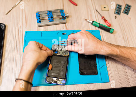 Mani di aggiustatore con pinzette su smontato smartphone durante lavori di riparazione Foto Stock