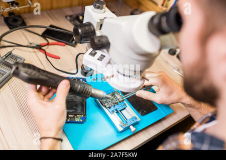 Mani di aggiustatore con utensili elettrici cercando nel microscopio durante il lavoro Foto Stock