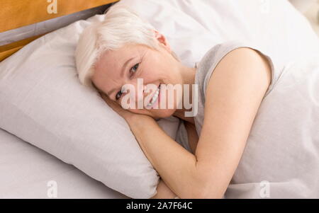 Ritratto di allegra donna senior in appoggio a letto Foto Stock