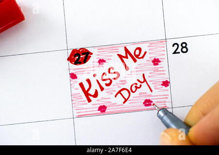 Dita di donna con penna scrittura promemoria Kiss Me giorno nel calendario. Agosto 27th. Close-up. Foto Stock
