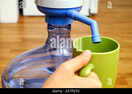 Donna con mano tazza verde vicino a bottiglia con pompa dell'acqua. Close-up. Foto Stock