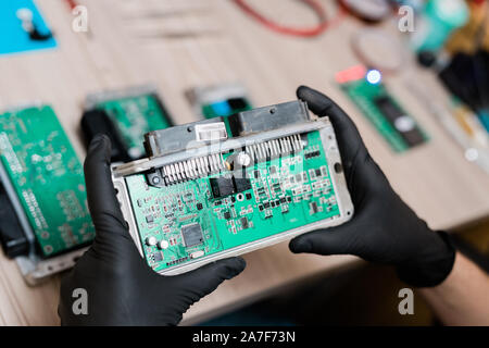 Anche se si indossano guanti di servizio di riparazione master esaminando una parte di smontata gadget Foto Stock