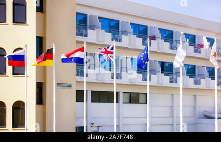 Russo, Olandese, Tedesco, Inglese, Greco, Cipro, Unione europea bandiere sui pennoni che fluttua nel vento di fronte all'hotel Foto Stock