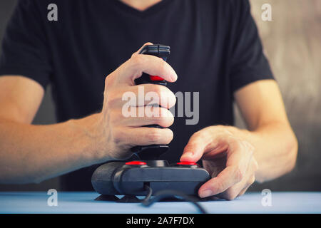 Giovane uomo la riproduzione del video gioco con un joystick retrò. Joystick per giochi a partire dalla metà degli anni ottanta. Il joystick ha particelle di polvere e di graffi. Foto Stock