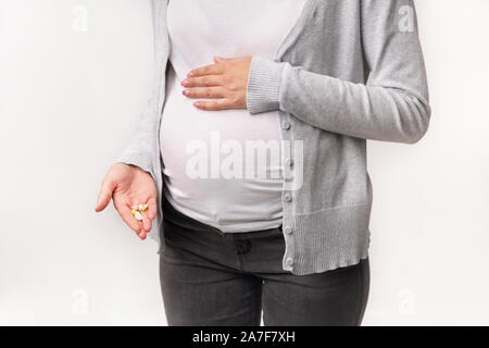 Irriconoscibile la donna incinta che mostra pillole toccando pancia in studio, ritagliato Foto Stock