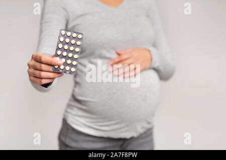 Irriconoscibile incinta ragazza mostra pillole Blister in piedi in Studio Foto Stock