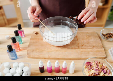 Giovane donna versando olio essenziale di piccola bottiglia di liquido nella massa di sapone Foto Stock