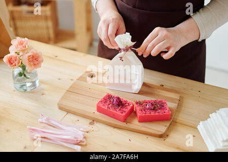 Le mani della donna decorazione pacchetto di carta con fiori mentre imballaggio sapone artigianale Foto Stock